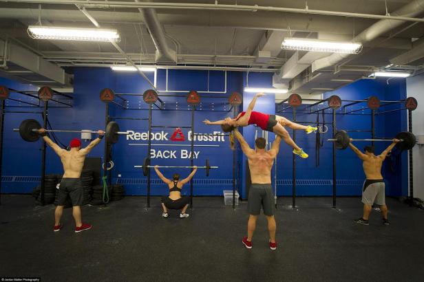 In einem Crossfit-Studio trainieren mehrere Personen mit Gewichten, während ein Mann eine Frau hochhebt.
