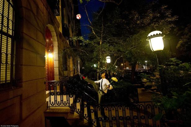 Ein Mann mit Blumen in der Hand balanciert auf einer Treppe vor einem Haus einen Fußball.