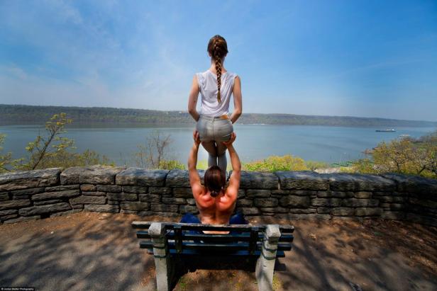Ein Mann hebt eine Frau auf einer Bank mit Blick auf einen Fluss hoch.