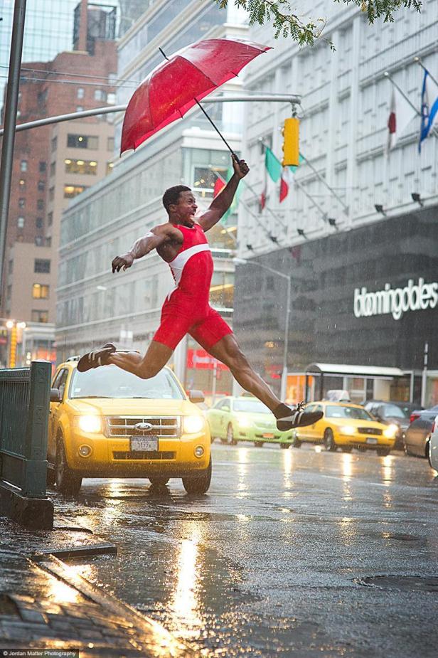 Ein Mann in Sportkleidung springt mit einem roten Regenschirm in der Hand über eine nasse Straße.