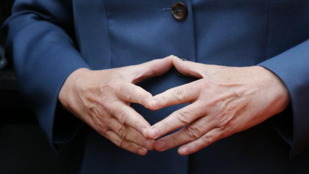 Die Hände einer Person in einer Geste vor einem blauen Blazer.