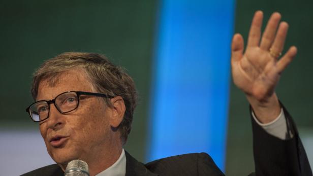Bill Gates spricht bei einer Veranstaltung und hebt seine Hand.