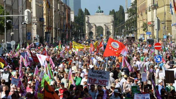 Eine große Menschenmenge demonstriert in München mit Fahnen und Transparenten in Richtung Siegestor.