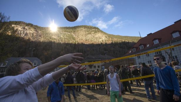 Menschen spielen Beachvolleyball vor einer bewaldeten Hügellandschaft.