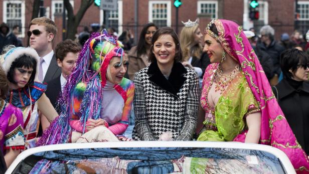 Marion Cotillard mit anderen Personen in auffälligen Kostümen auf einer Parade.