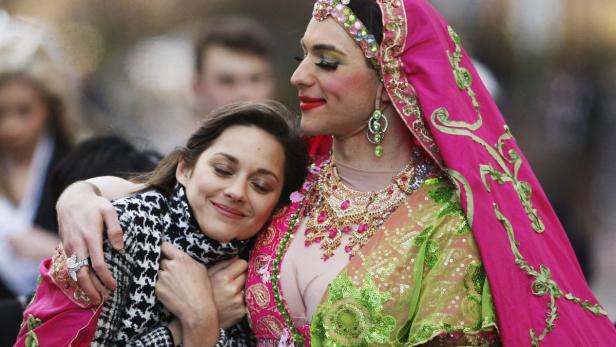 Marion Cotillard umarmt einen Mann in einem farbenprächtigen, indisch inspirierten Kostüm.