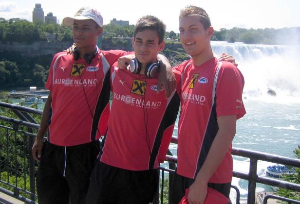 Drei junge Männer in Sporttrikots posieren vor den Niagarafällen.