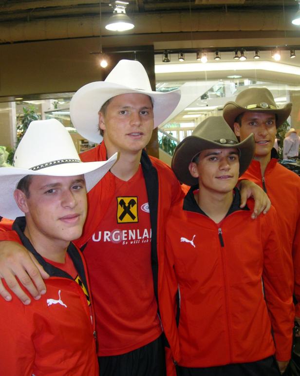 Vier junge Männer in roten Trainingsjacken und Cowboyhüten posieren für ein Foto.