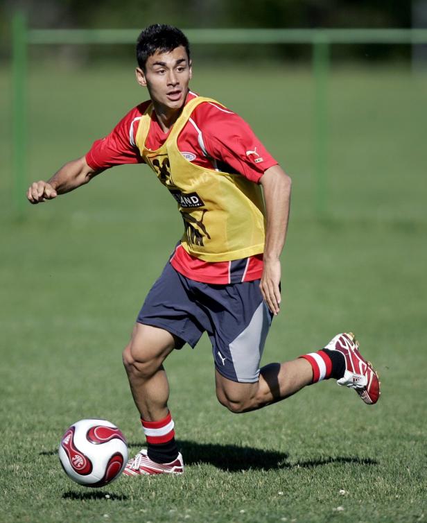 Ein Fußballspieler in rotem Trikot dribbelt einen Ball auf einem grünen Rasen.