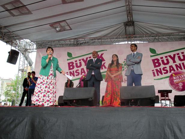 Eine Frau spricht auf einer Bühne mit Mikrofon, flankiert von drei weiteren Personen.