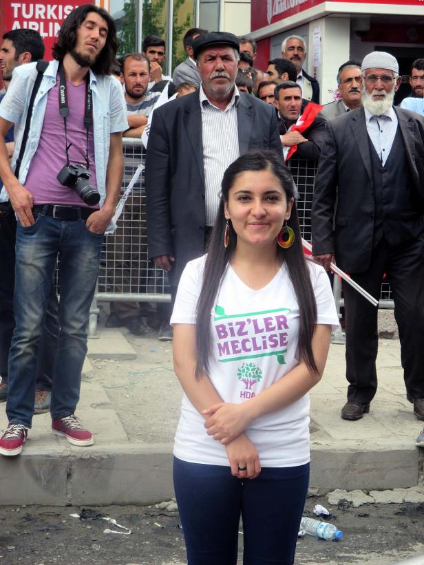 Eine junge Frau mit einem T-Shirt der HDP-Partei steht vor einer Menschenmenge.