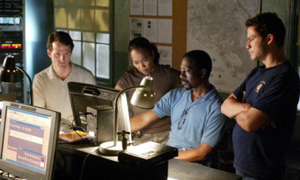 Vier Personen arbeiten in einem Büro mit Computern und Karten an der Wand.