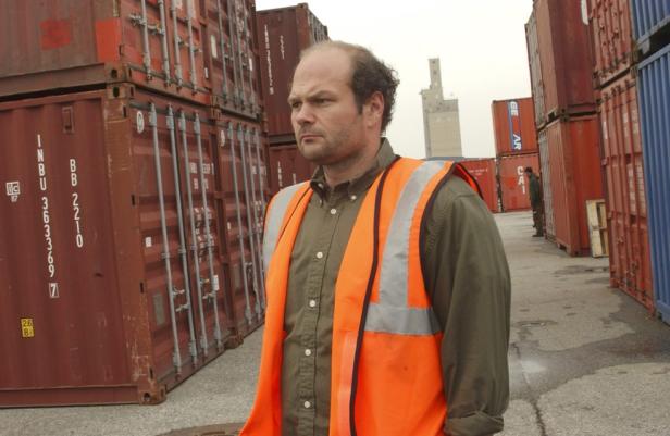 Ein Mann mit Warnweste steht zwischen roten Containern.