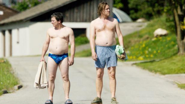 Zwei Männer in Badehose stehen auf einer Straße.