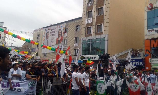 Eine Menschenmenge demonstriert auf der Straße mit Flaggen und Bannern vor einem Gebäude.