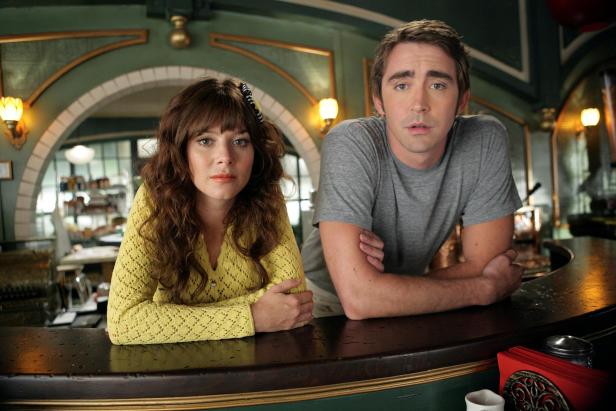 Anna Friel und Lee Pace stehen an einer Theke.