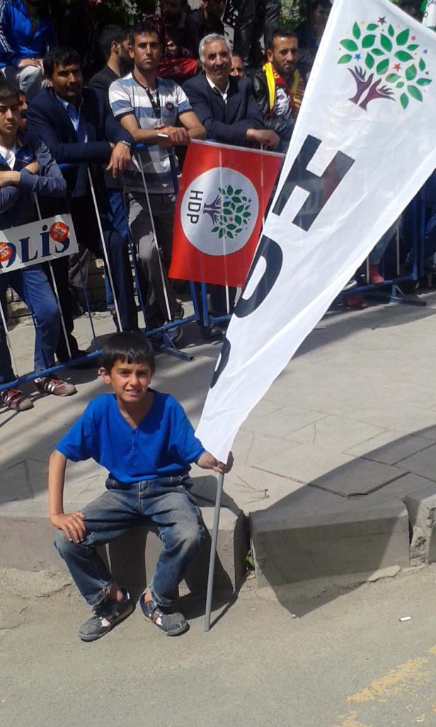 Ein Junge sitzt mit einer HDP-Flagge am Straßenrand.