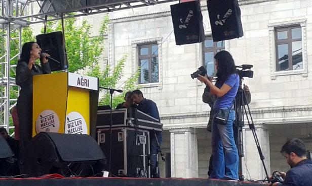 Eine Frau spricht auf einer Bühne vor Publikum, während andere filmen.