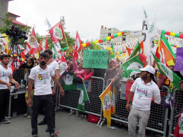 Eine Menschenmenge demonstriert mit HDP-Flaggen und Schildern, auf denen „0 Baraj Yikilacak“ steht.