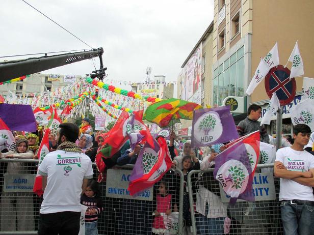 Eine Menschenmenge demonstriert mit HDP-Flaggen und Transparenten in einer städtischen Umgebung.