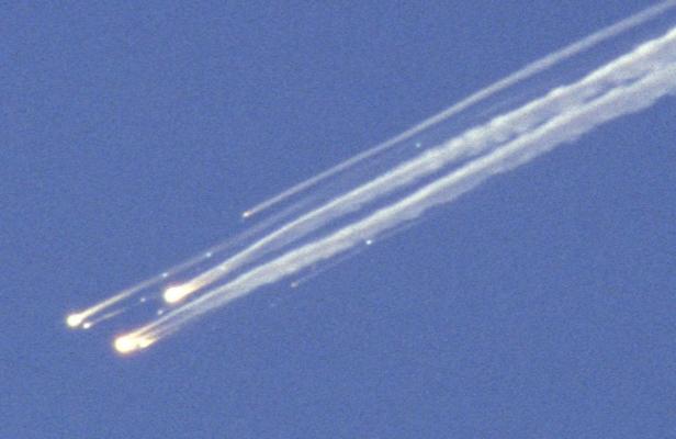Mehrere Trümmerteile fallen mit Rauchfahnen vom Himmel.
