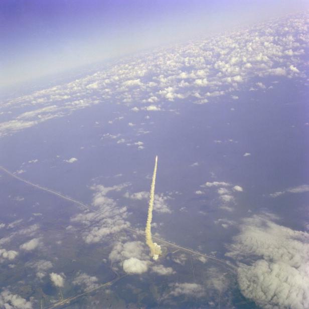 Eine Rakete steigt mit einer Rauchfahne in den Himmel auf, gesehen aus der Vogelperspektive.