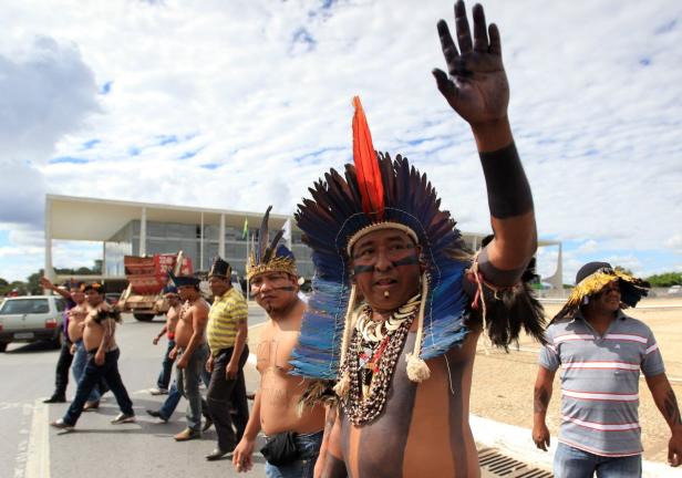 Eine Gruppe indigener Demonstranten in traditioneller Kleidung marschiert auf einer Straße.
