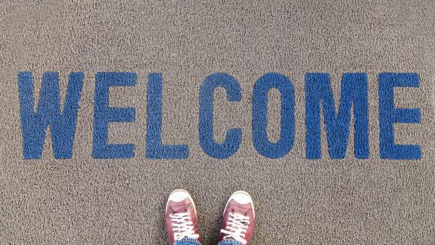 Ein Paar Füße steht auf einer Fußmatte mit der blauen Aufschrift „Welcome“.