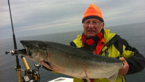 Ein Mann mit orangefarbener Mütze hält einen großen Fisch auf einem Boot.