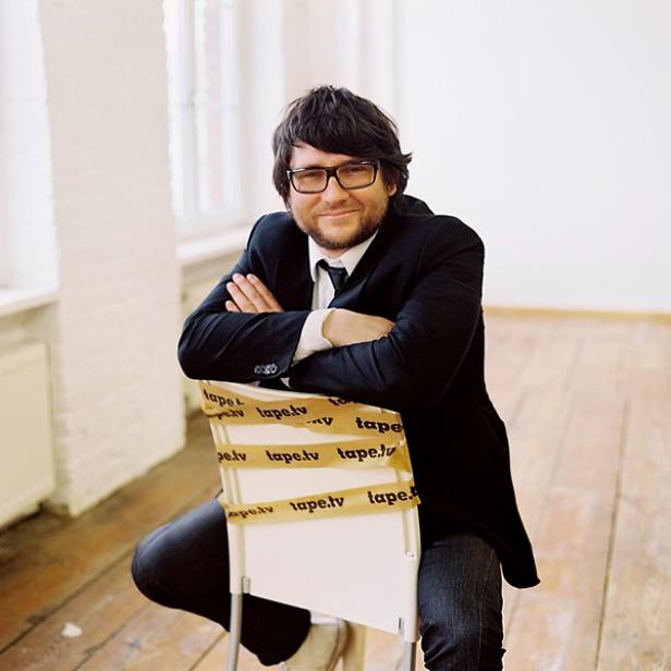 Ein Mann mit Brille und Anzug sitzt auf einem mit Klebeband umwickelten Stuhl.