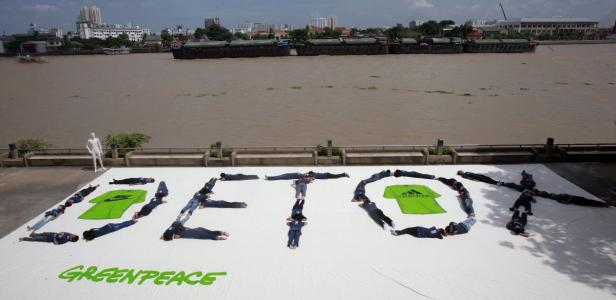 Menschen liegen auf einem Banner und formen das Wort „Detox“ mit Greenpeace-Logo und T-Shirts von Nike und Adidas.