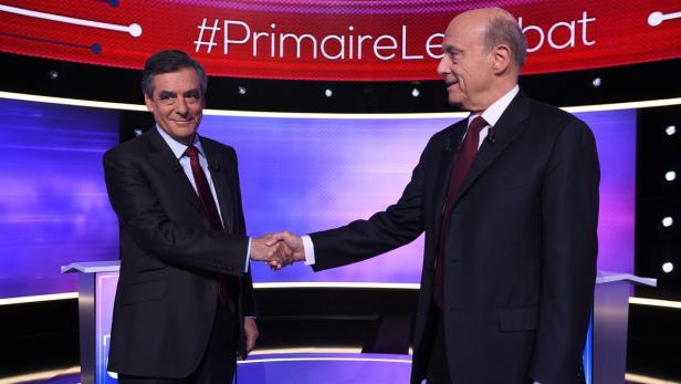 François Fillon und ein weiterer Mann schütteln sich vor dem Hintergrund der „Primaire Le Débat“.