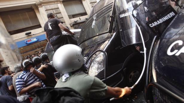 Demonstranten stehen vor Polizeiwagen der Carabinieri in einer Stadt.