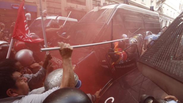 Eine Menschenmenge demonstriert vor Polizeiwagen inmitten von rotem Rauch.