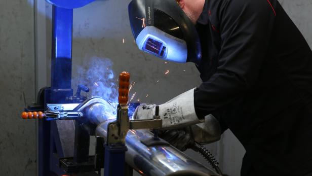 Ein Schweißer arbeitet mit Schutzmaske an einem Metallrohr.