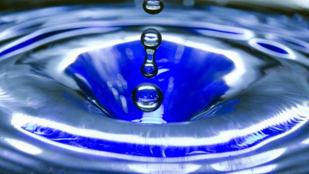 Ein Wassertropfen fällt in eine mit blauem Wasser gefüllte Oberfläche und erzeugt Wellen.