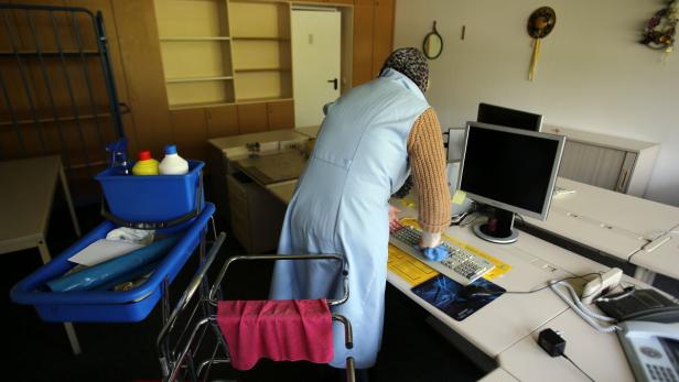 Eine Reinigungskraft putzt einen Schreibtisch mit Computer und Telefon.