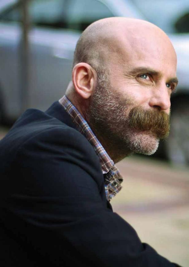 Ein Mann mit Bart und Schnurrbart blickt zur Seite.