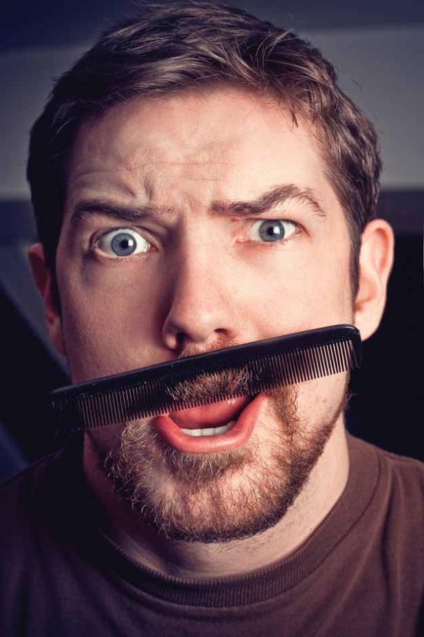 Ein Mann hält einen Kamm vor sein Gesicht und verzieht es komisch.