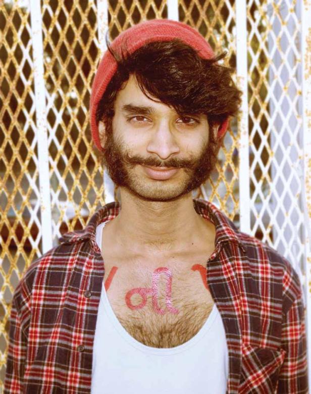 Ein Mann mit Bart und Mütze steht vor einem Gitter.