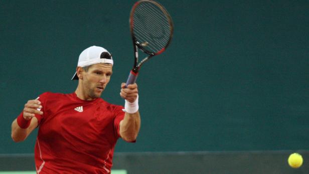 Ein Tennisspieler in rotem Hemd schlägt einen Ball.