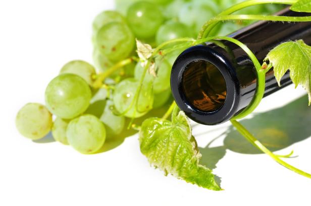 Eine Flasche Wein liegt neben einer Traube grüner Weintrauben.