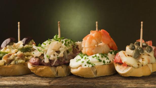 Eine Auswahl von vier verschiedenen Tapas auf Brot, garniert mit Gemüse, Fleisch und Meeresfrüchten.