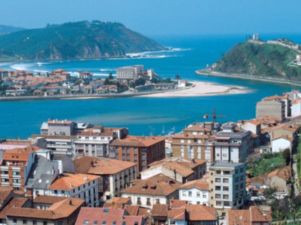 Blick auf eine Stadt mit roten Dächern an einer Flussmündung zum Meer.