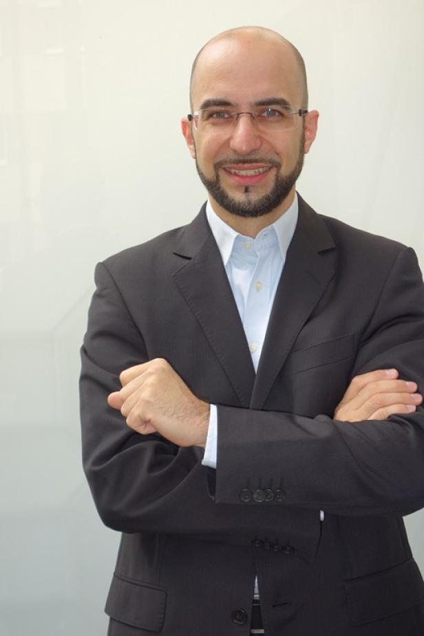 Ein Mann mit Brille und Anzug lächelt mit verschränkten Armen in die Kamera.