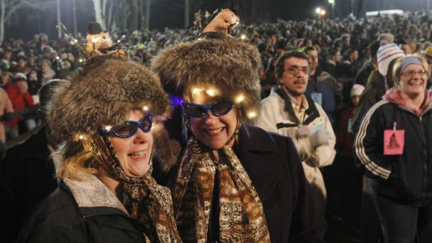 Zwei Frauen mit Fellmützen und blauen Brillen stehen in einer Menschenmenge.