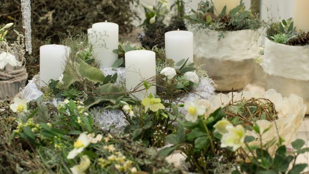 Oh du blühende Adventzeit Gestecke mit weißen Kerzen, Blumen und winterlichen Dekorationen stehen auf einem Tisch.