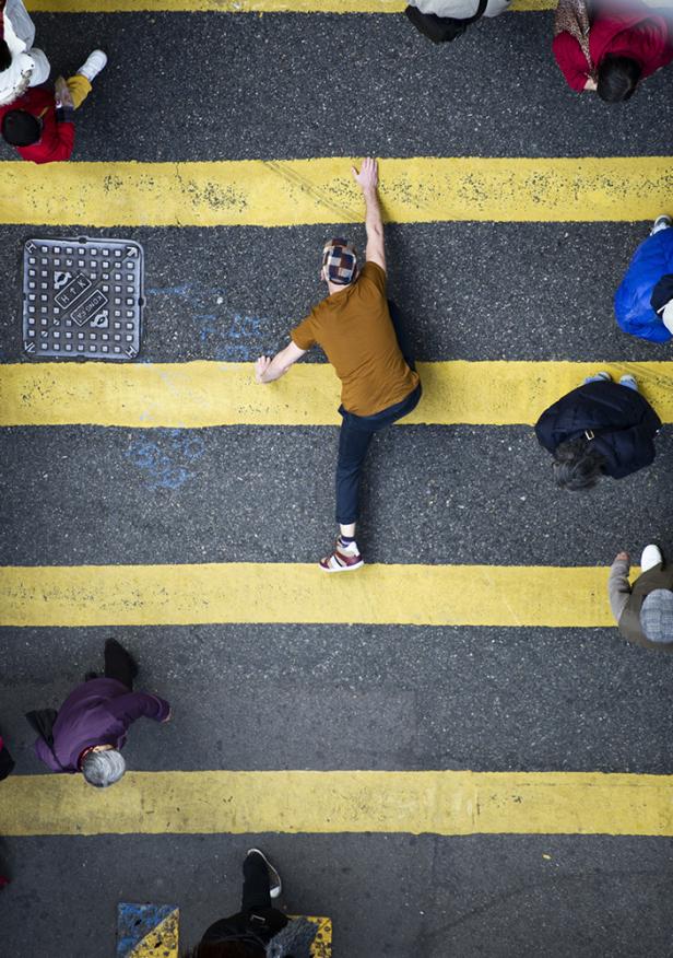 Ein Mann balanciert auf einer gelb markierten Straße, umgeben von Passanten.