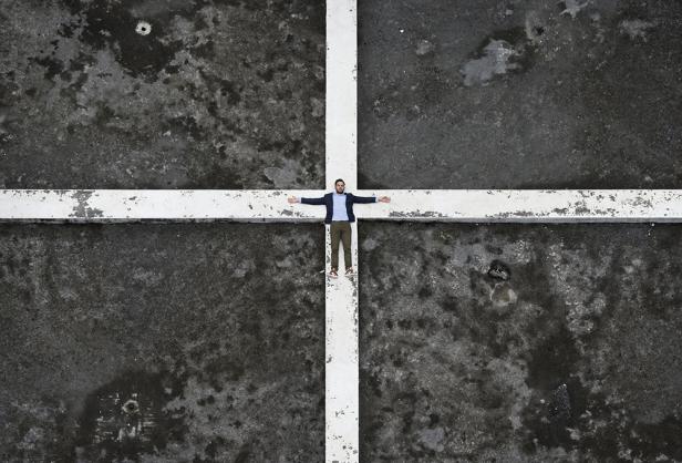 Ein Mann liegt mit ausgestreckten Armen auf einem weißen Kreuz auf einem dunklen Untergrund.