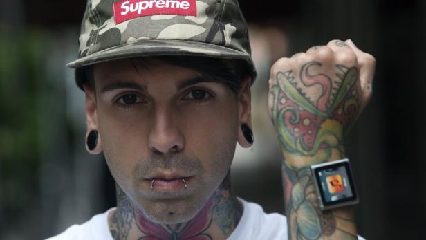 Ein Mann mit Tattoos, Tunnel-Ohrringen und einer Kappe mit „Supreme“-Logo zeigt seine Smartwatch.